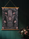 Botanical Hamsa wall tapestry featuring intricate rose gold and teal design on black background, showing a protective hand symbol surrounded by leaf motifs and floral elements, hanging from wooden dowels with natural twine.